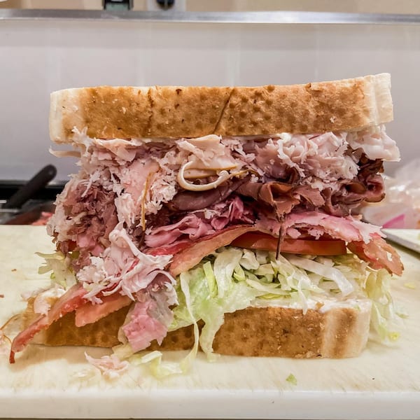 A large, deli-style sandwich with generous layers of meat, lettuce, and tomato on white bread.