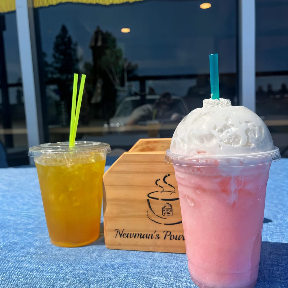 Two drinks, a yellow iced tea and a pink blended drink with whipped cream, on a blue table.