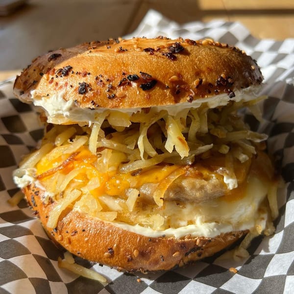 Everything bagel sandwich with cream cheese, egg, cheese, and hash browns in checkered paper.