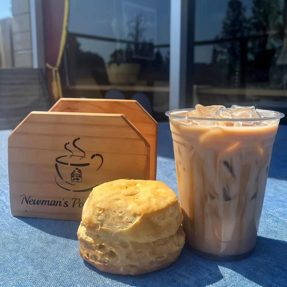 Iced coffee, a biscuit, and a wooden napkin holder with Newman's Pour and Pies logo on a blue table.