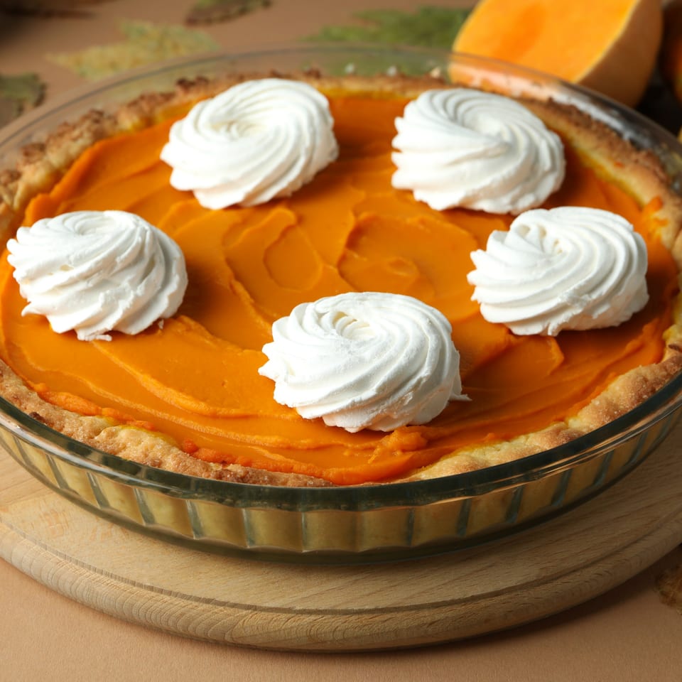 A vibrant orange pumpkin pie with five dollops of white whipped cream, in a glass dish.